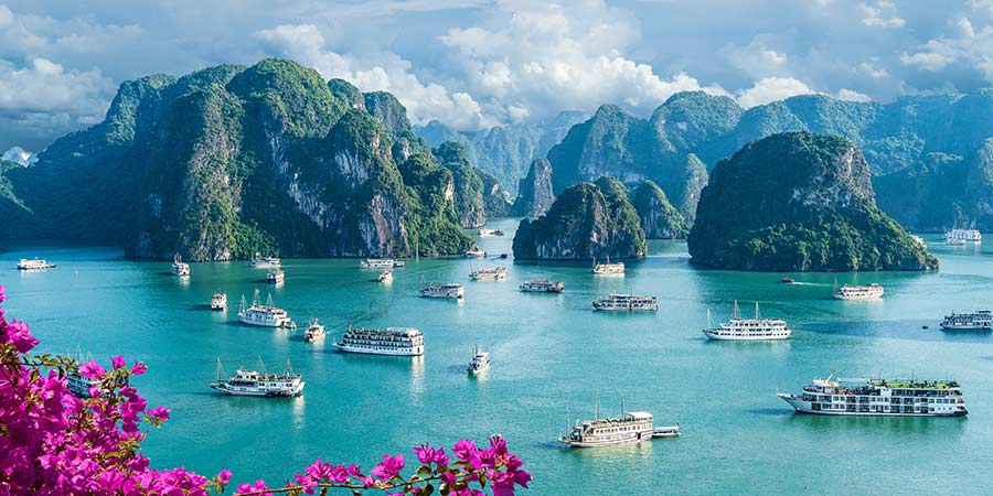 The beautiful turquoise waters of Ha Long Bay are dotted with white boats and small rocky islands. 